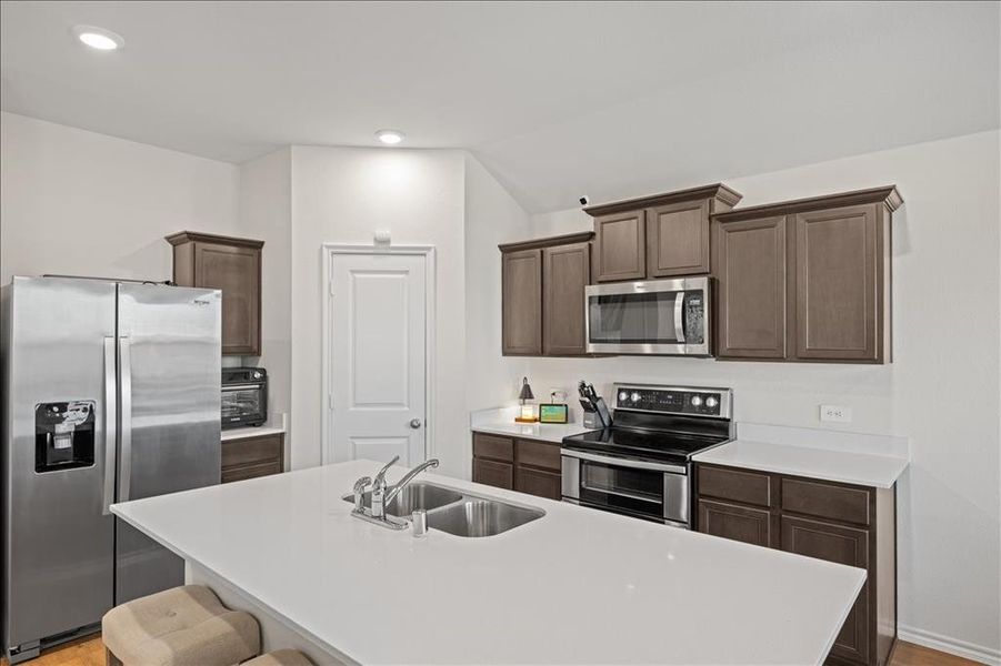 Kitchen featuring appliances with stainless steel finishes, dark brown cabinets, an island with sink, a kitchen breakfast bar, and light wood-style flooring Kitchen featuring appliances with stainless steel finishes, dark brown cabinets, an island with sink, a kitchen breakfast bar, and light wood-style flooring