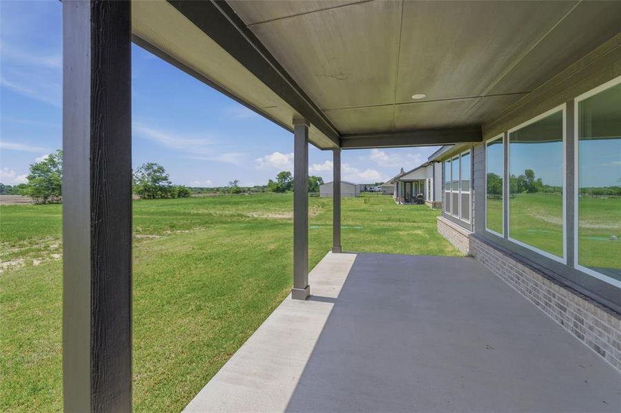 Covered concrete patio with recessed lighting, bordered by a textured dark gray column and a brick facade Covered concrete patio with recessed lighting, bordered by a textured dark gray column and a brick facade