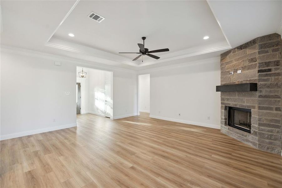 Unfurnished living room with a fireplace, light hardwood / wood-style floors, crown molding, ceiling fan, and a raised ceiling