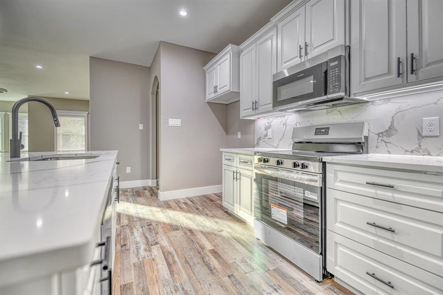 Kitchen with appliances with stainless steel finishes, light stone counters, recessed lighting, backsplash, and arched walkways
