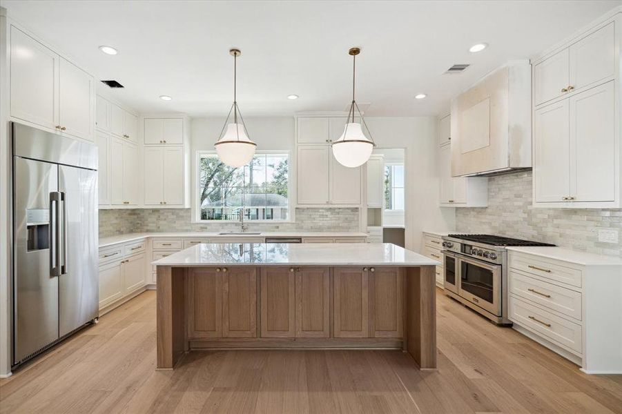 Clean lines and timeless elegance define this chef-inspired kitchen. Custom cabinetry extends to the ceiling, providing ample storage, while the soft-toned backsplash adds texture and depth. The oversized island, crafted with natural wood tones and topped with pristine quartz, serves as a functional centerpiece for meal prep and gathering. High-end stainless appliances, including a double oven and a built-in refrigerator, elevate the space, while large windows invite in natural light and offer serene views.