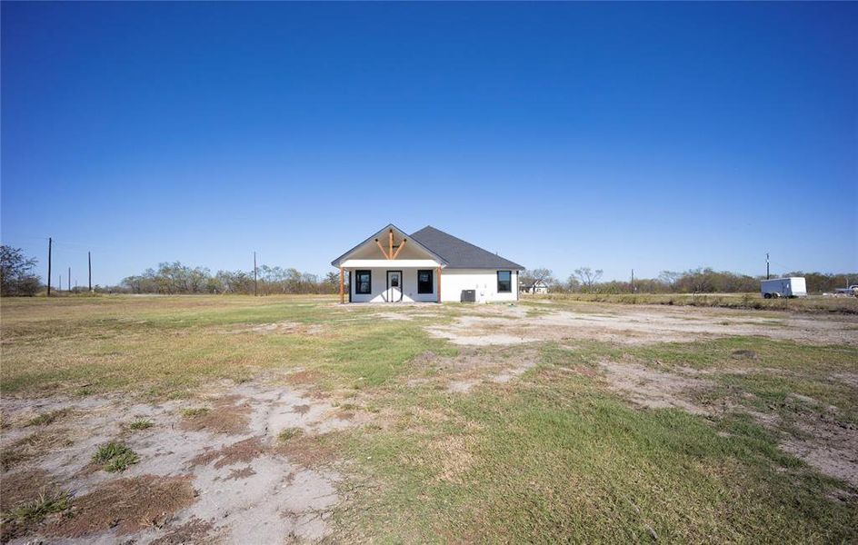 Back of house with covered porch, a view of countryside, and a yard