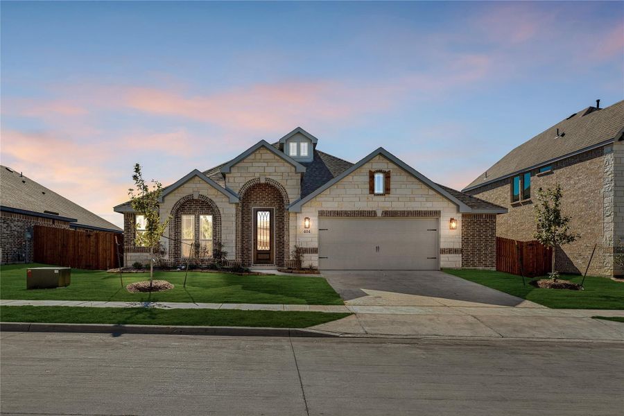 Single-story home with stone and brick exterior, arched entry, two-car garage, and green front lawn at dusk