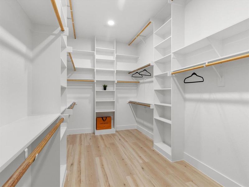 Expansive walk-in closet featuring light wood-finish flooring, white built-in shelving, multiple hanging rods, recessed lighting, and crisp white baseboards Expansive walk-in closet featuring light wood-finish flooring, white built-in shelving, multiple hanging rods, recessed lighting, and crisp white baseboards