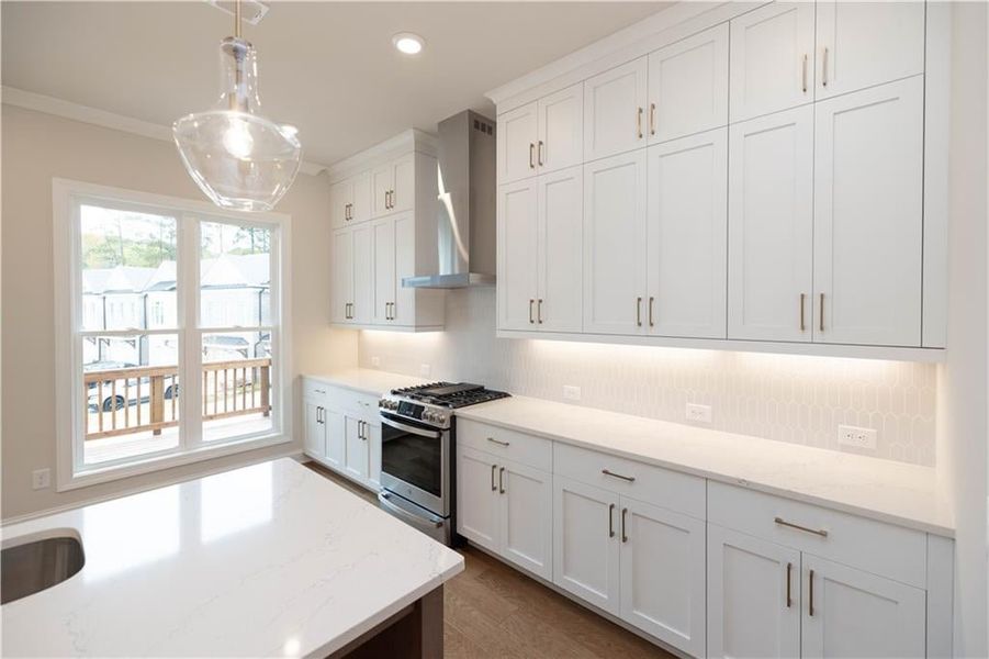 Kitchen featuring pendant lighting, backsplash, stainless steel range with gas stovetop, white cabinets, and wall chimney exhaust hood