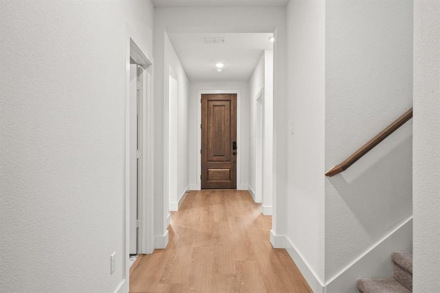 Hallway with light wood-style flooring, a textured wall, and stairway Hallway with light wood-style flooring, a textured wall, and stairway