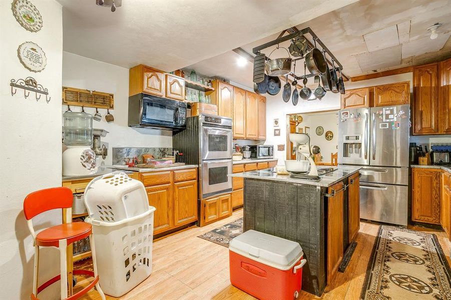 Kitchen featuring light wood finished floors, stainless steel appliances, a center island, and brown cabinetry Kitchen featuring light wood finished floors, stainless steel appliances, a center island, and brown cabinetry