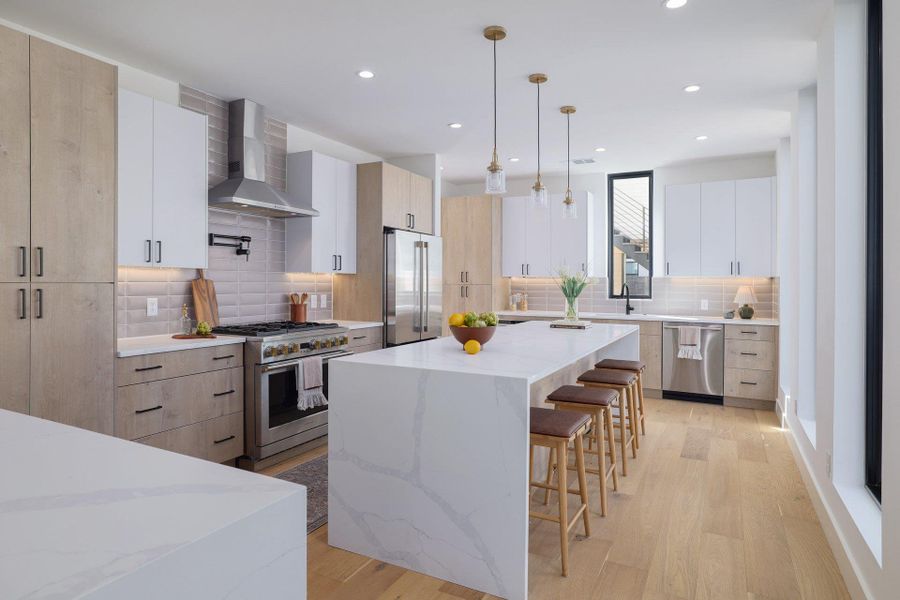 Kitchen with two tone cabinets, pendant lighting, high end appliances, light stone counters, and a center island