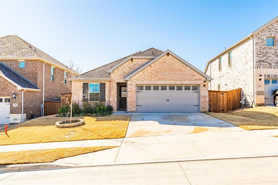 Traditional-style house with an attached garage, brick siding, a shingled roof, fence, and concrete driveway