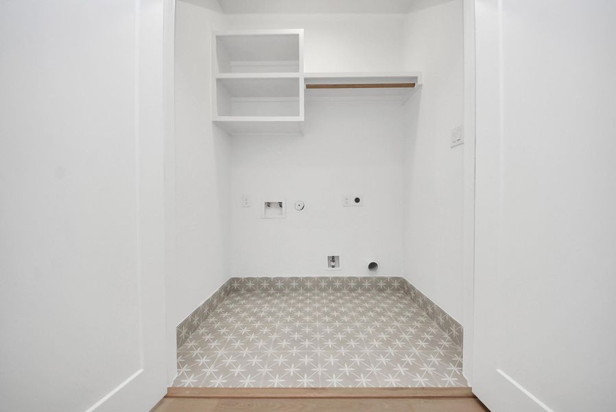 A compact yet functional laundry nook with washer and dryer hookups, built-in shelving, and a hanging rod for added storage. Patterned tile flooring adds a stylish, modern touch.