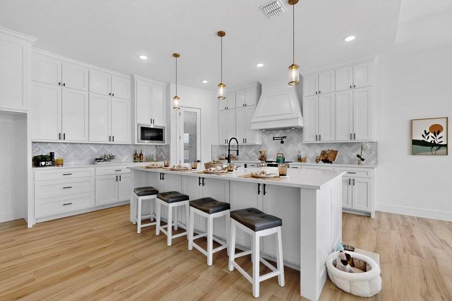 Kitchen with a breakfast bar area, white cabinets, hanging light fixtures, light wood-style floors, and recessed lighting Kitchen with a breakfast bar area, white cabinets, hanging light fixtures, light wood-style floors, and recessed lighting
