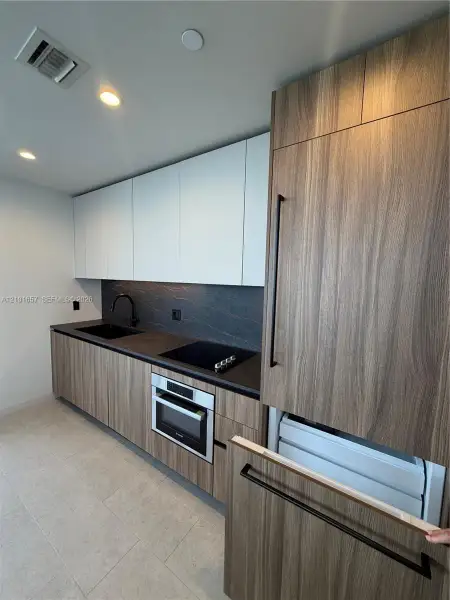 Kitchen featuring wood-finish cabinetry, matte black hardware, integrated appliance paneling, dark stone-finish countertops, and a stone-finish backsplash