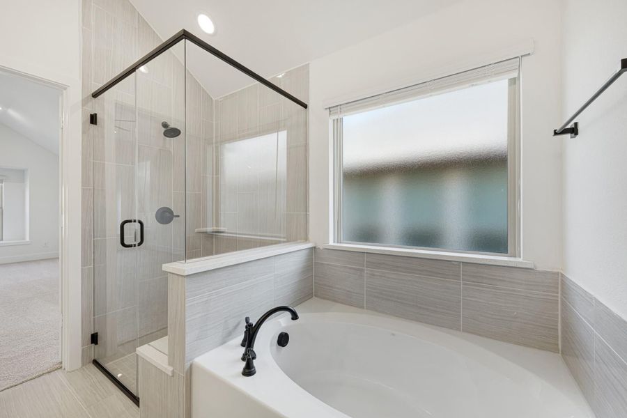 Ensuite bathroom with soaking tub, glass-enclosed shower, gray tile walls, and frosted window