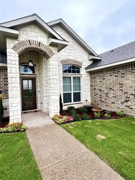 View of exterior entry featuring stone siding, a lawn, and brick siding View of exterior entry featuring stone siding, a lawn, and brick siding