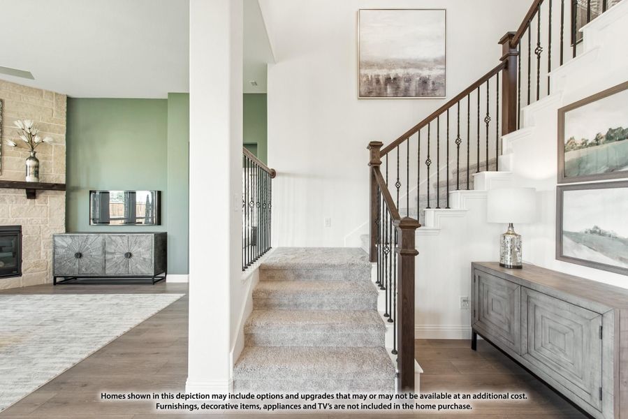 Carpeted staircase with dark wood and iron railings, open to living room with stone fireplace and hardwood floors Carpeted staircase with dark wood and iron railings, open to living room with stone fireplace and hardwood floors