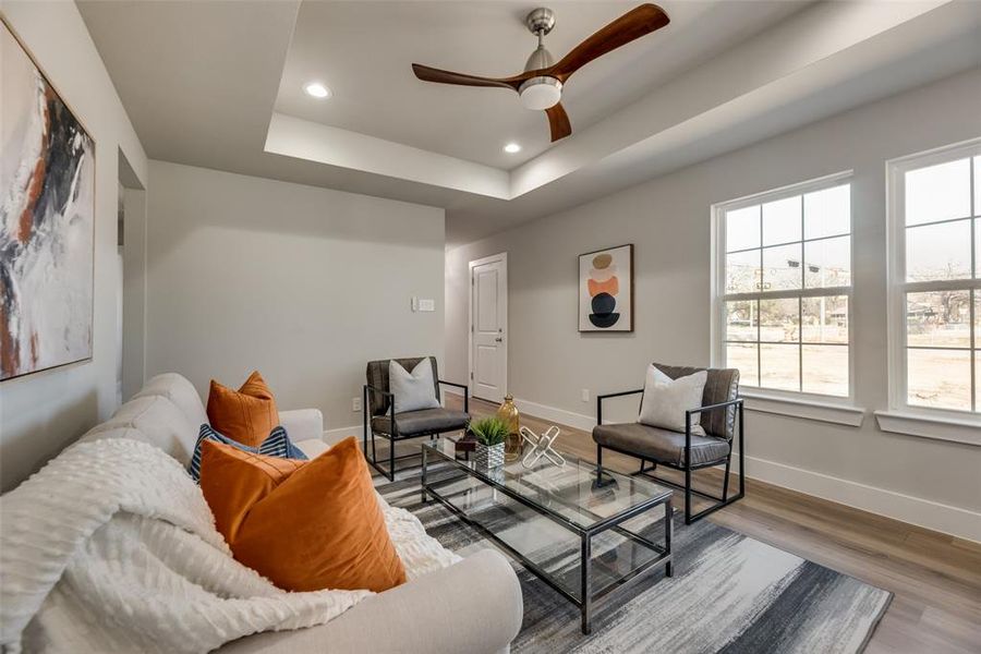 Living room featuring wood-type flooring, ceiling fan, and a tray ceiling