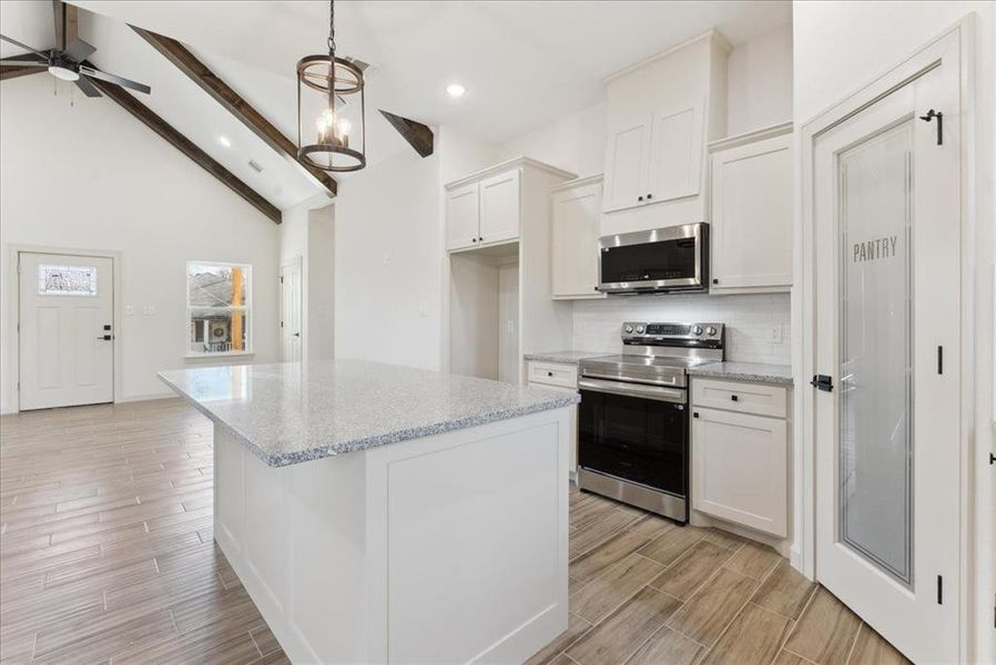 Kitchen with hanging light fixtures, a kitchen island, appliances with stainless steel finishes, beam ceiling, and white cabinetry