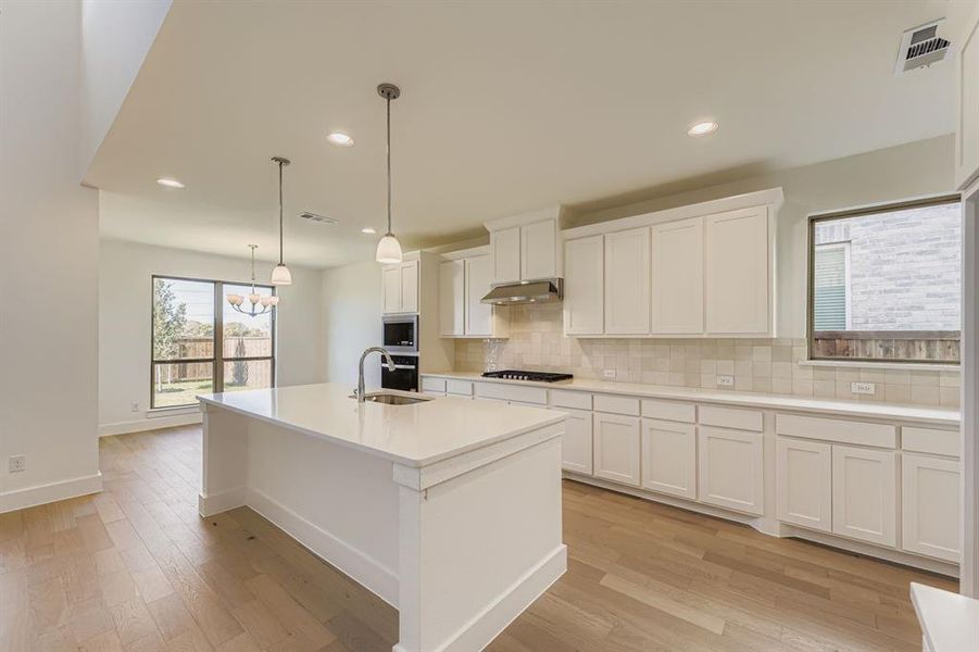 Kitchen featuring white cabinets, tasteful backsplash, a kitchen island with sink, light wood-style flooring, and recessed lighting Kitchen featuring white cabinets, tasteful backsplash, a kitchen island with sink, light wood-style flooring, and recessed lighting