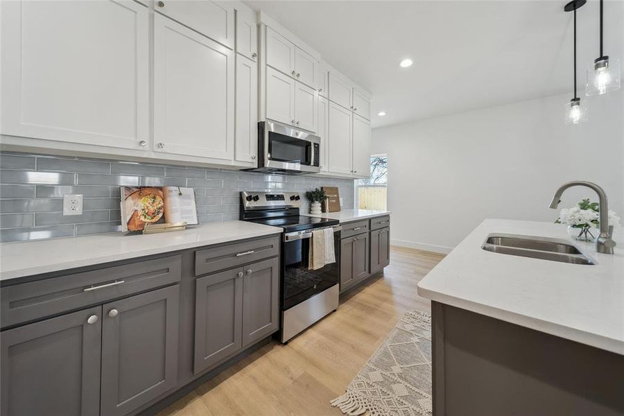 Kitchen with white cabinetry, stainless steel appliances, sink, and pendant lighting