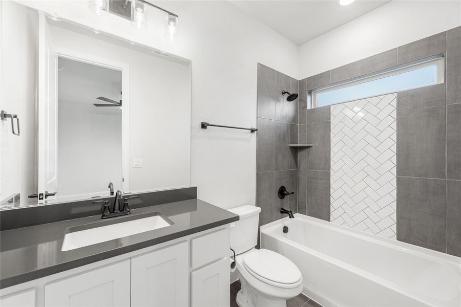 Bathroom with white vanity, gray countertop, and tiled tub-shower combo with herringbone accent tile