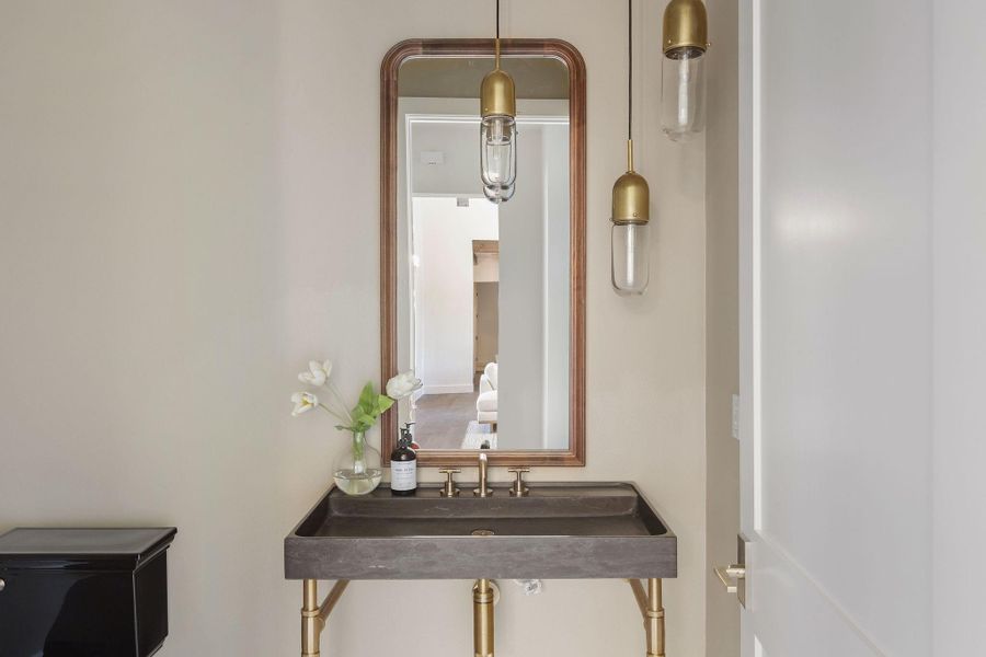 Half bathroom downstairs for guests with Stone Vessel Sink with Brass Legs and Faucet, White Penny Tile Flooring, and Walnut Framed Vanity Mirror