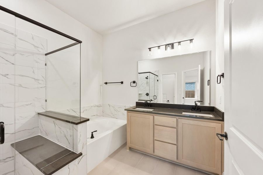 Bathroom with double sink vanity, soaking tub, marble tile surround, and glass shower enclosure with black fixtures