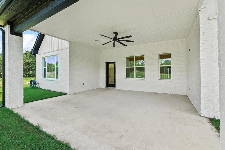 Expansive covered patio featuring a concrete surface, white brick exterior, black ceiling fan, and multiple windows Expansive covered patio featuring a concrete surface, white brick exterior, black ceiling fan, and multiple windows