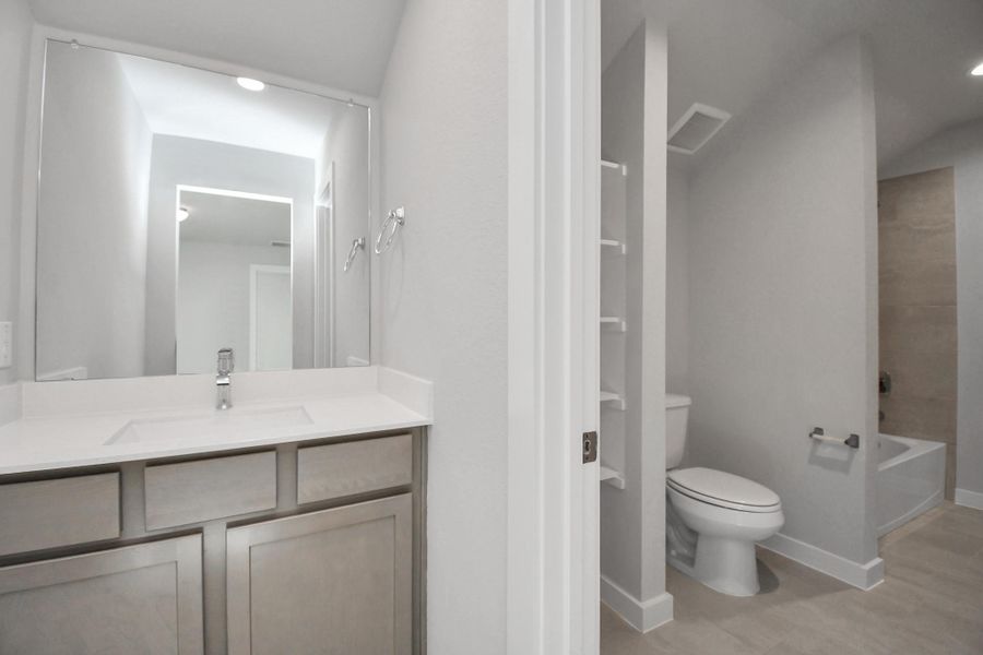 Experience convenience in the secondary bathroom, designed for Jack and Jill arrangements, now with a separate vanity area. This well-appointed space showcases stylish tile flooring, a bath/shower combo with an elegant tile surround, and light-stained wood cabinets. The beautiful light countertop adds a touch of sophistication, combining functionality and aesthetics seamlessly. Experience convenience in the secondary bathroom, designed for Jack and Jill arrangements, now with a separate vanity area. This well-appointed space showcases stylish tile flooring, a bath/shower combo with an elegant tile surround, and light-stained wood cabinets. The beautiful light countertop adds a touch of sophistication, combining functionality and aesthetics seamlessly.