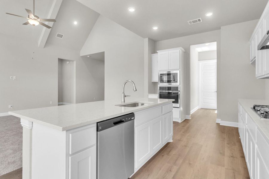 Kitchen with appliances with stainless steel finishes, white cabinets, a kitchen island with sink, light stone counters, and ceiling fan
