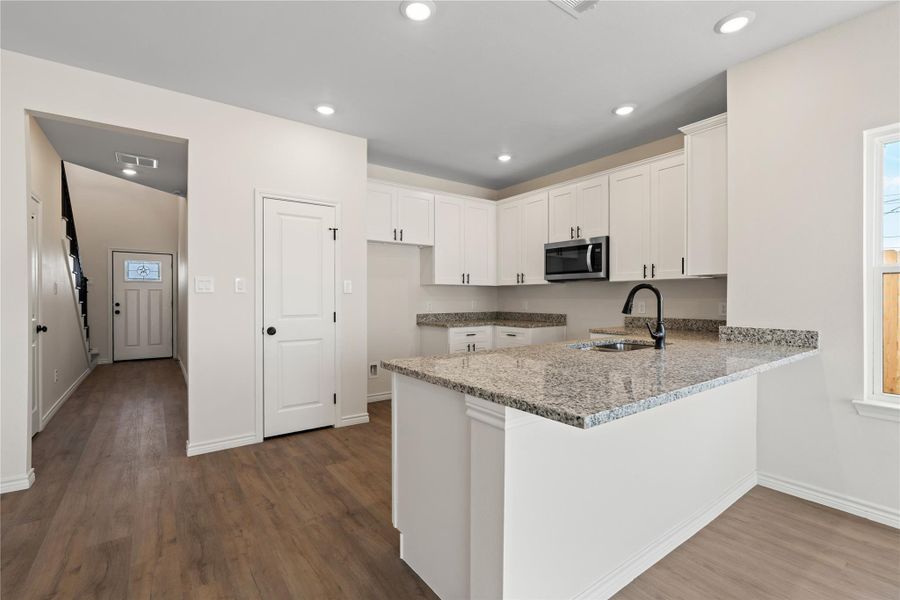 Bright and functional, the kitchen features white shaker-style cabinetry, speckled granite countertops, and matte black hardware for a crisp modern farmhouse look.