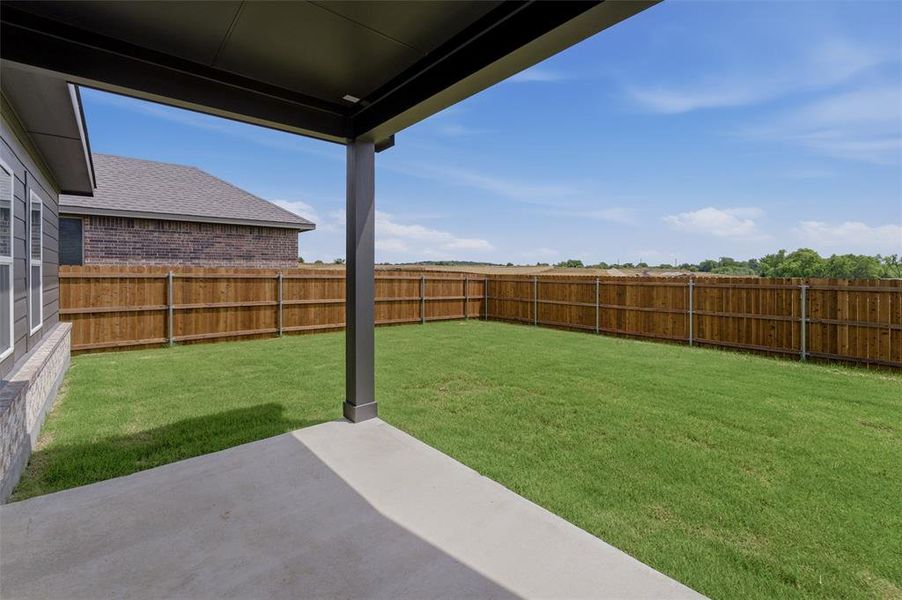 Expansive backyard featuring a concrete patio, covered porch area, and a privacy fence