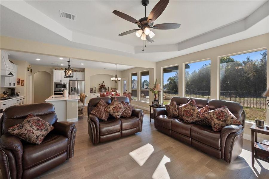 Living room with a raised ceiling, a chandelier, arched walkways, a ceiling fan, and light wood-style flooring Living room with a raised ceiling, a chandelier, arched walkways, a ceiling fan, and light wood-style flooring