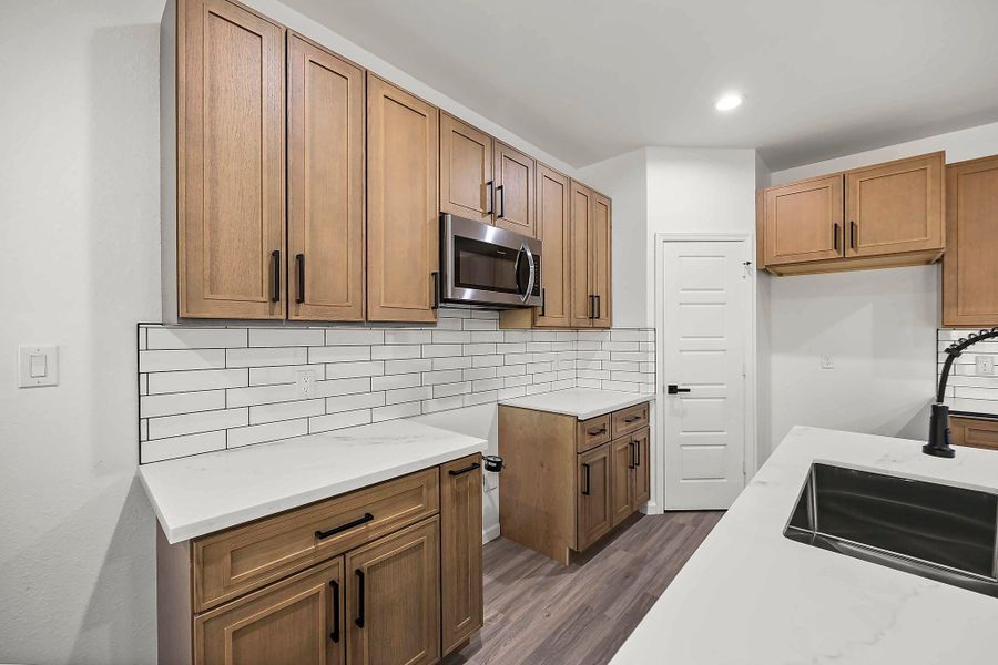 Sleek kitchen featuring modern wood cabinetry, stainless steel appliances, and elegant white countertops with a subway tile backsplash.