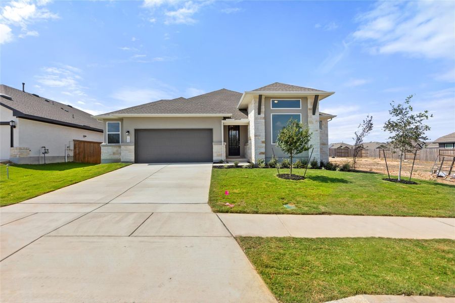 Prairie-style home featuring concrete driveway, an attached garage, a shingled roof, stucco siding, and stone siding