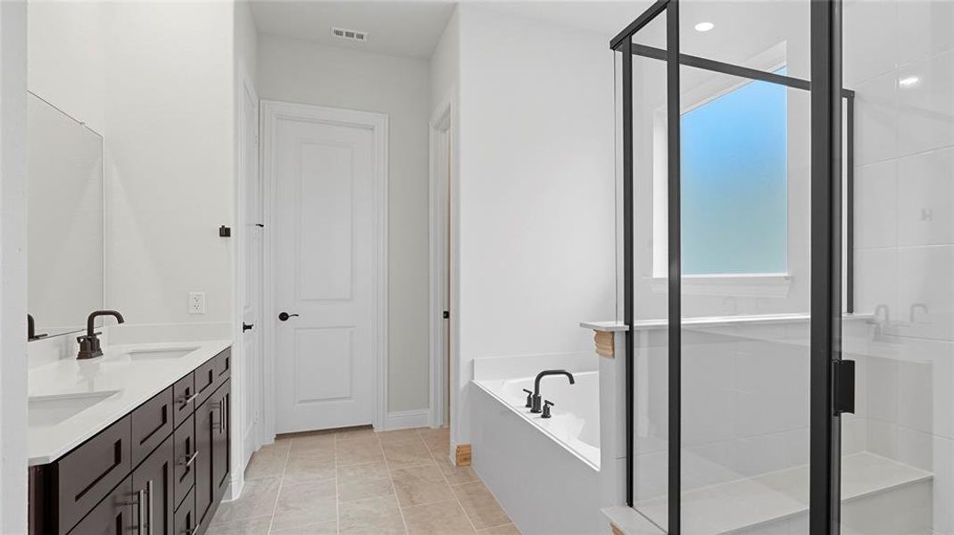 Bathroom featuring a dark wood double vanity with white countertops, a built-in tub, a separate shower with black-framed glass enclosure, and tiled flooring
