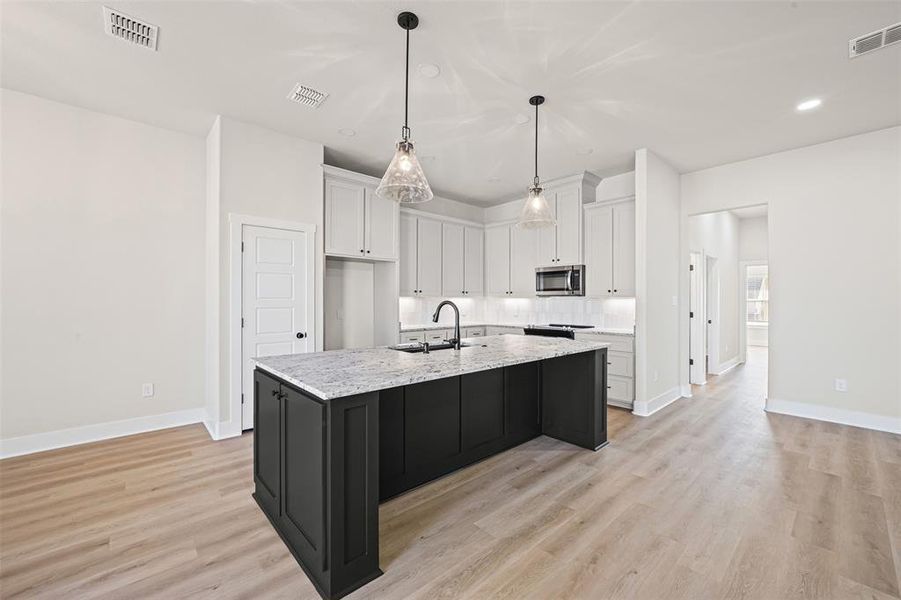 Kitchen with white cabinetry, dark cabinetry, pendant lighting, light stone countertops, and a kitchen island with sink Kitchen with white cabinetry, dark cabinetry, pendant lighting, light stone countertops, and a kitchen island with sink