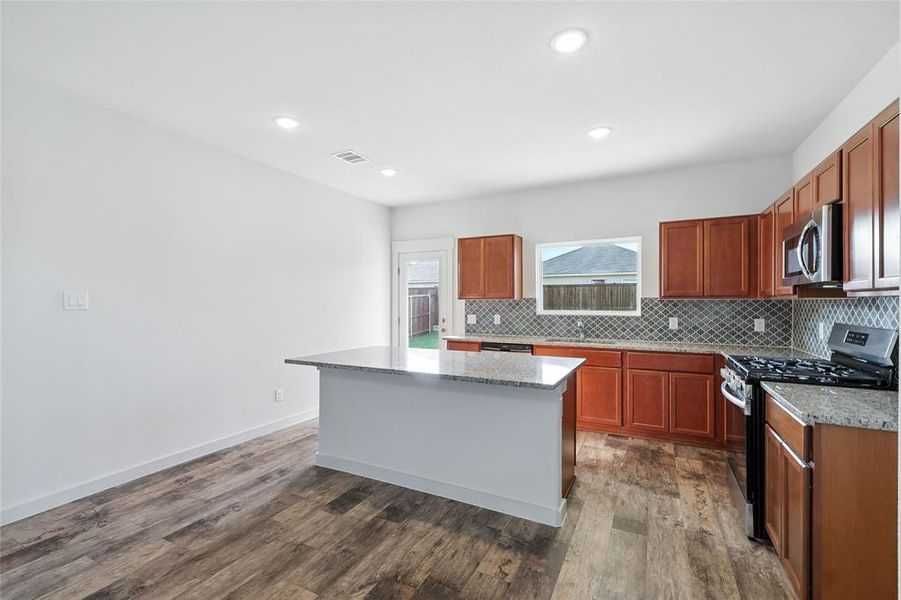 Kitchen featuring tasteful backsplash, appliances with stainless steel finishes, a kitchen island, brown cabinets, and recessed lighting Kitchen featuring tasteful backsplash, appliances with stainless steel finishes, a kitchen island, brown cabinets, and recessed lighting