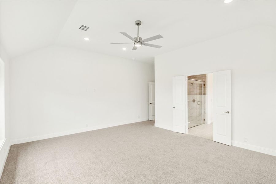 Spacious bedroom with vaulted ceiling, ceiling fan, carpet flooring, and ensuite bathroom with glass shower.