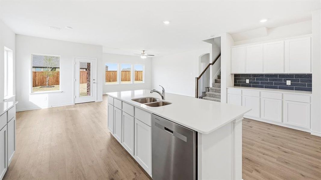 Kitchen with dishwasher, white cabinetry, an island with sink, decorative backsplash, and light wood-type flooring