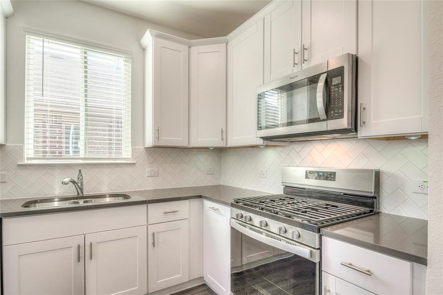 Kitchen featuring stainless steel appliances, white cabinetry, backsplash, and dark stone countertops Kitchen featuring stainless steel appliances, white cabinetry, backsplash, and dark stone countertops