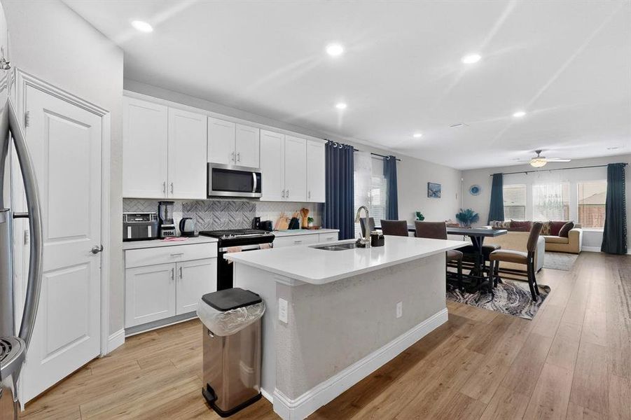 Kitchen with open floor plan, a center island with sink, stainless steel appliances, white cabinetry, and recessed lighting Kitchen with open floor plan, a center island with sink, stainless steel appliances, white cabinetry, and recessed lighting