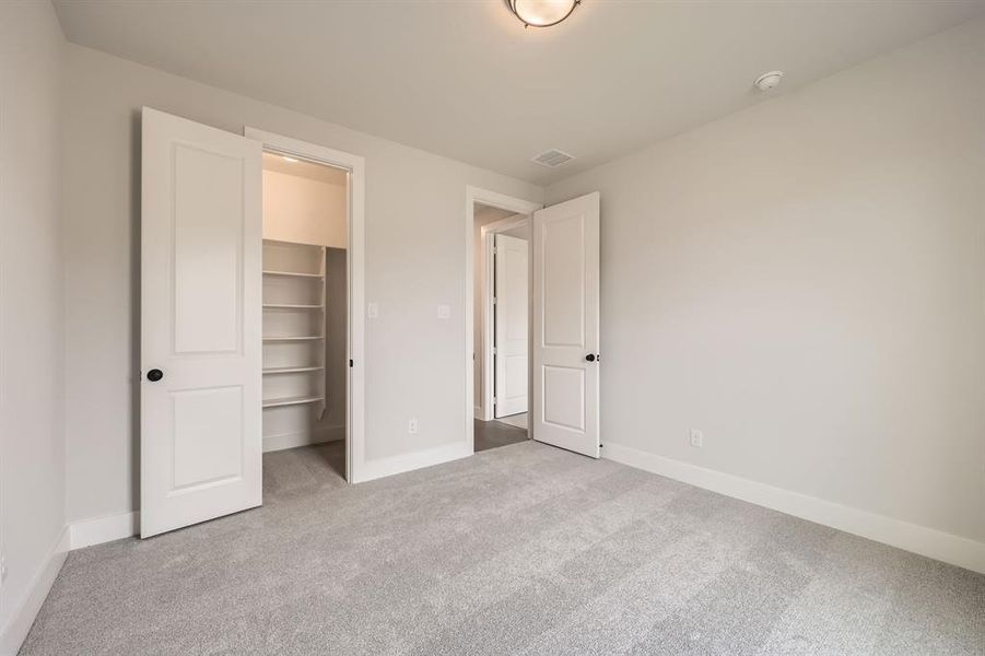 Unfurnished bedroom with a walk in closet, carpet, baseboards, visible vents, and a closet Unfurnished bedroom with a walk in closet, carpet, baseboards, visible vents, and a closet