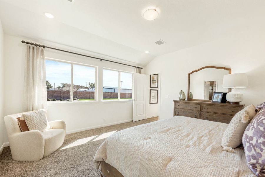 Bedroom with carpet flooring, wood dresser, accent chair, and large windows with backyard view