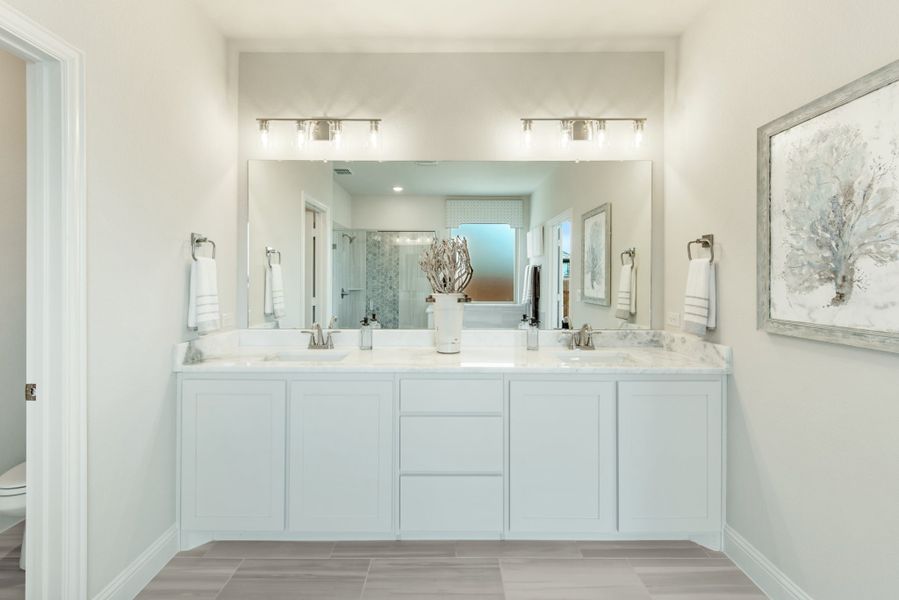 Bathroom with double vanity, white cabinets, marble countertops, and large mirror with overhead lighting