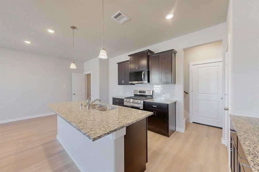 Kitchen featuring stainless steel appliances, dark brown cabinets, tasteful backsplash, light wood-style flooring, and hanging light fixtures