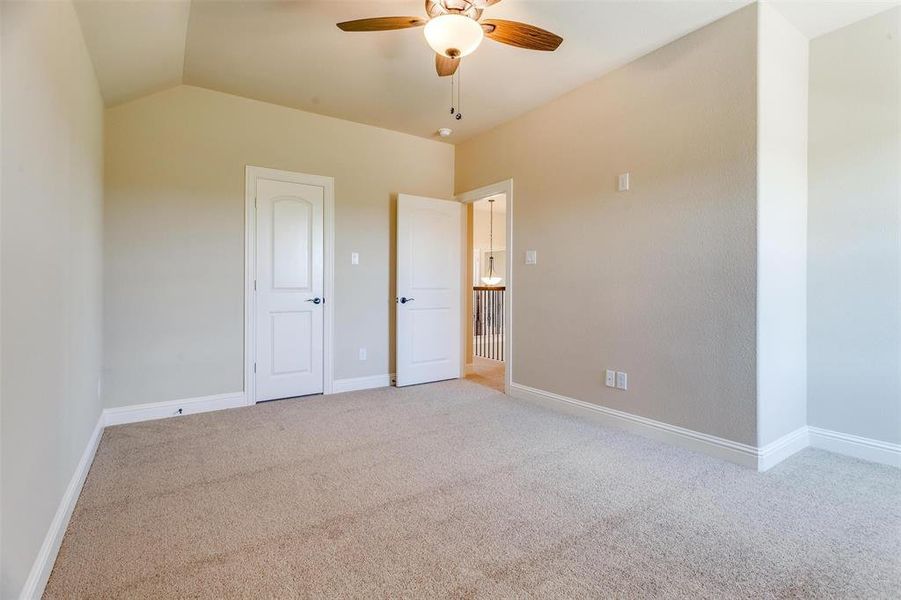 Unfurnished bedroom featuring ceiling fan, light colored carpet, and lofted ceiling