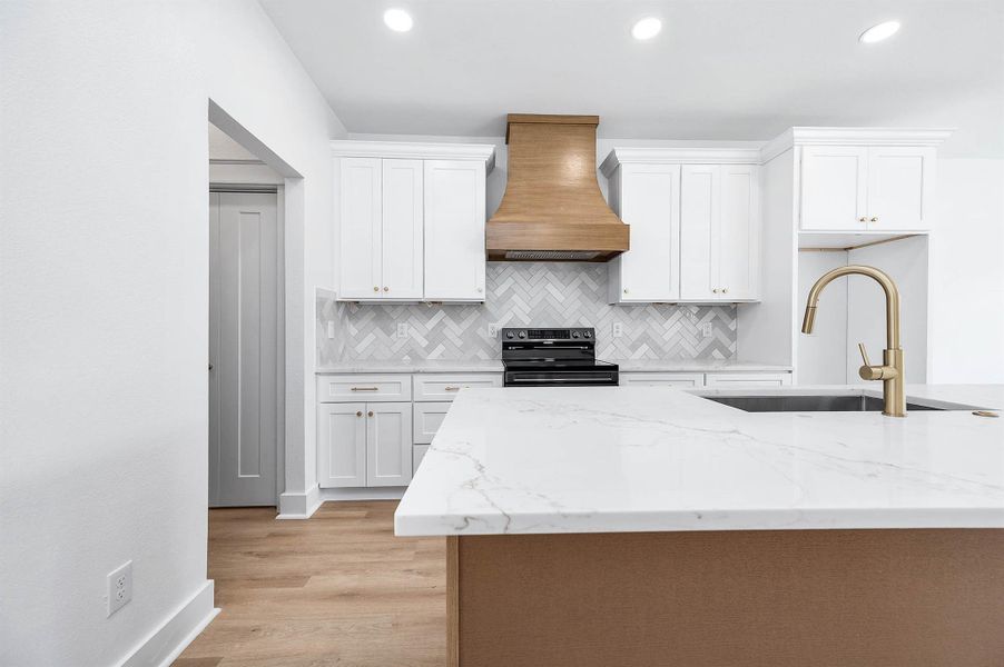 Quartz island with gold fixtures, custom wood vent hood, and a herringbone backsplash create a bright, modern kitchen centerpiece. Quartz island with gold fixtures, custom wood vent hood, and a herringbone backsplash create a bright, modern kitchen centerpiece.