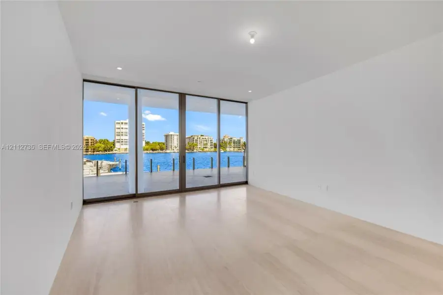 Floor-to-ceiling sliding glass panels with metal framing, wood-finish flooring, and expansive water exposure