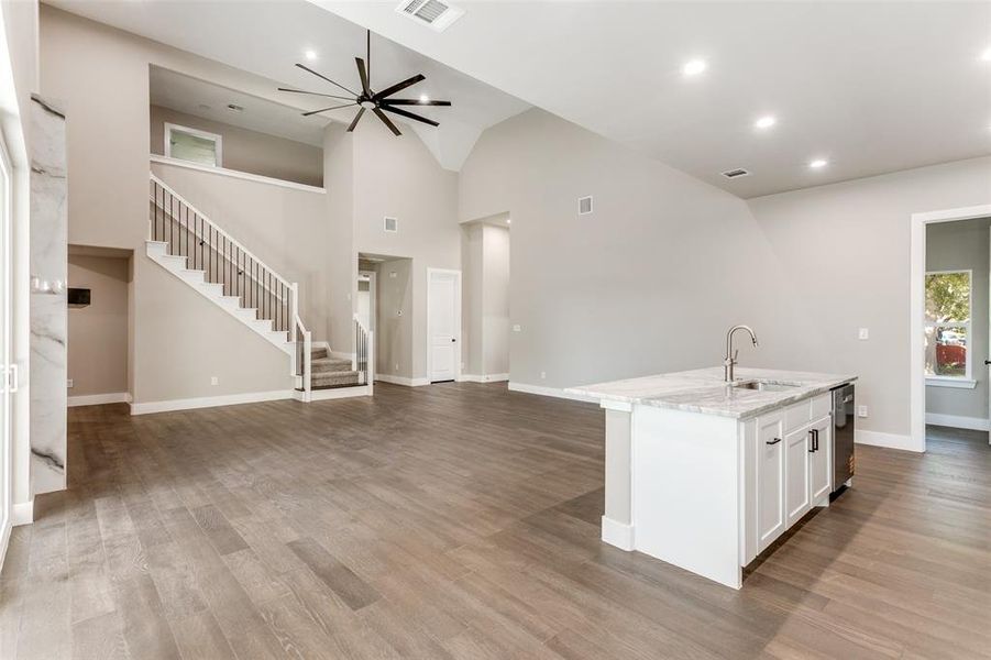 Kitchen featuring ceiling fan, open floor plan, white cabinetry, light stone countertops, and a center island with sink