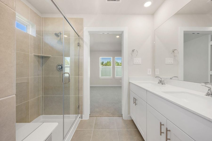 The primary bath features a sleek double vanity, a spacious glass-enclosed shower, and modern tile finishes throughout. Bright and inviting, this space combines comfort and style for a truly relaxing retreat.